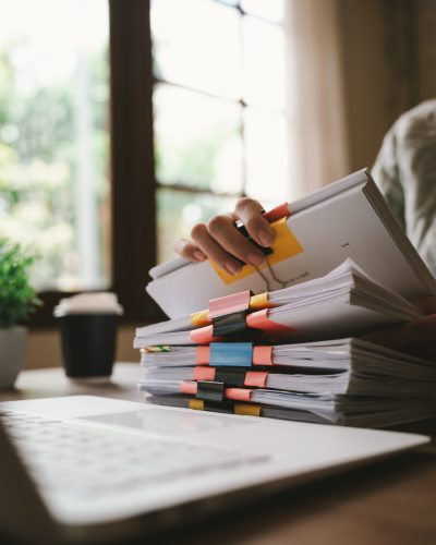A close-up shot of an Asian woman handling a large volume of documents and files, dealing with organization, management, deadlines, workload, bureaucracy, and business responsibilities.