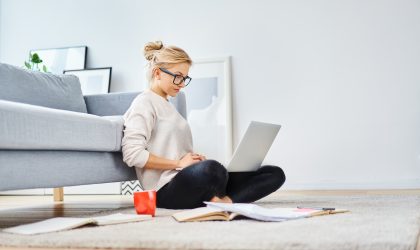 Young woman sitting on floor at home working with laptop and documents