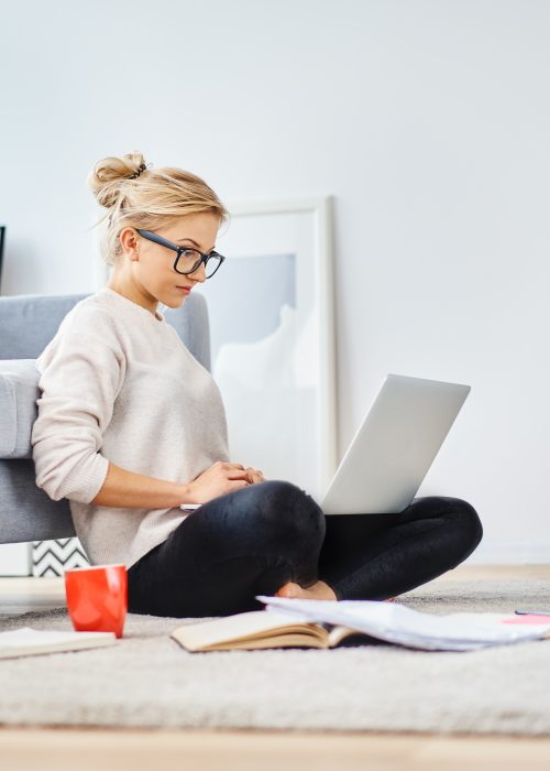 Young woman sitting on floor at home working with laptop and documents