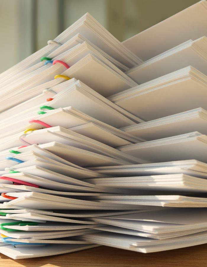 High stack of office documents with clips on office table close up. Concept of overworking and paperwork in office.