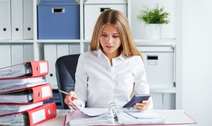Beautiful business woman calculates tax at desk in office